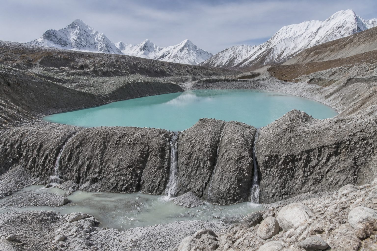 A glacial lake held by a fragile moraine dam in the high Himalayas, water seeping through cracks.