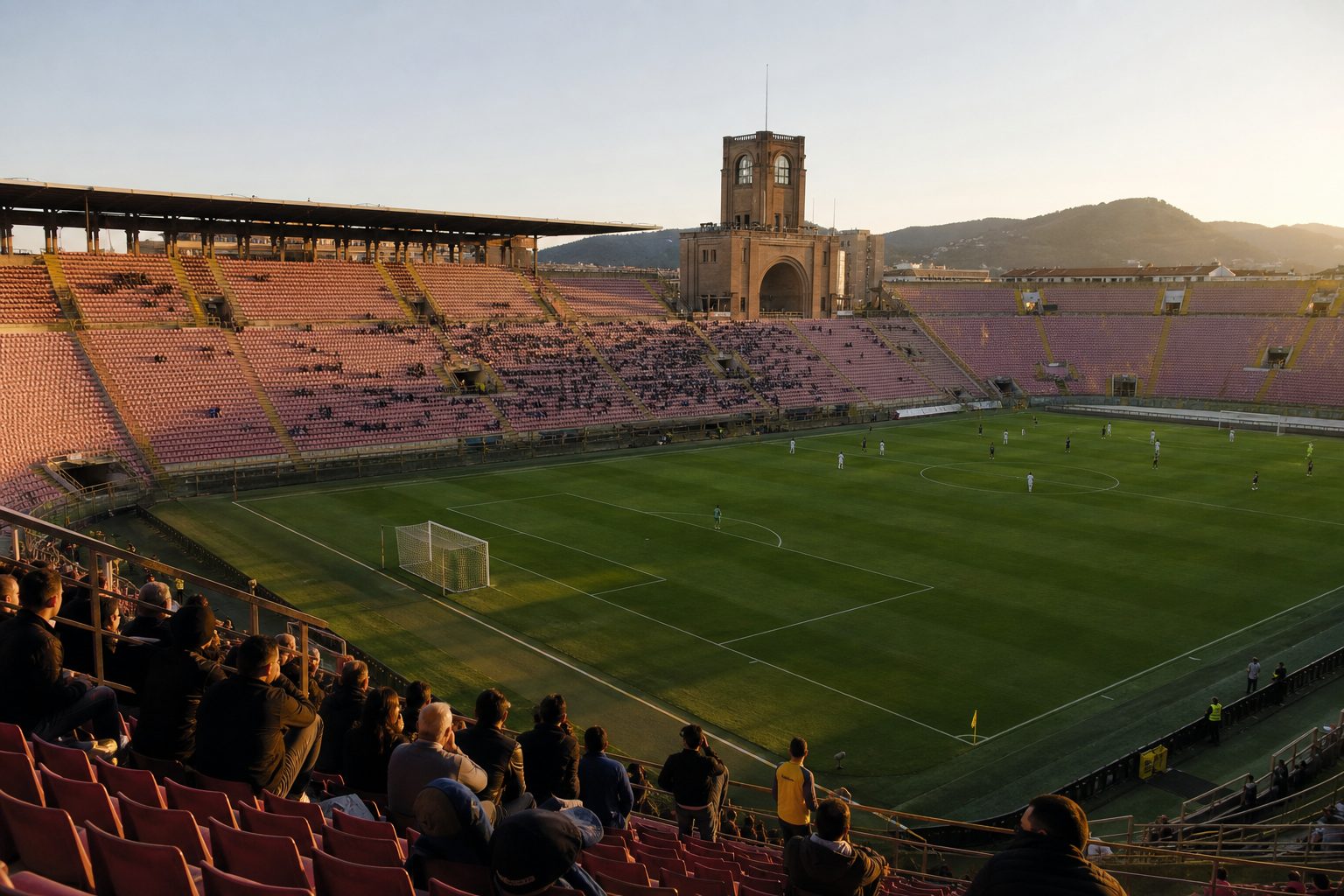 A historic European football stadium in late afternoon sunlight, its older architecture and continental design clearly visible.