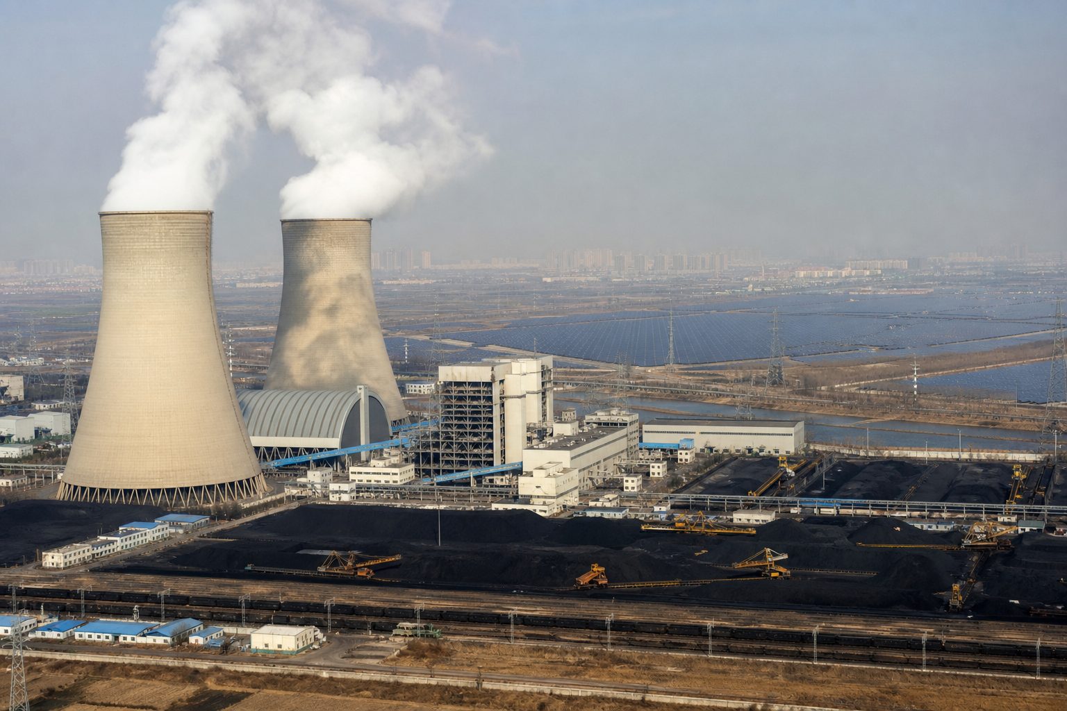 Coal power plant cooling towers with a solar panel array visible on the plain behind them.