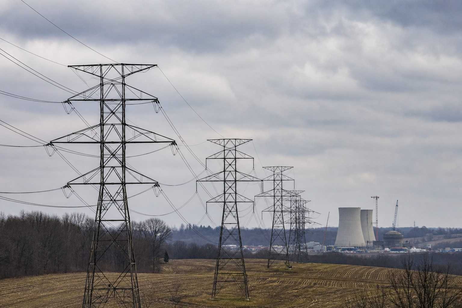 High-voltage transmission towers crossing rural Ohio toward a distant industrial construction site.