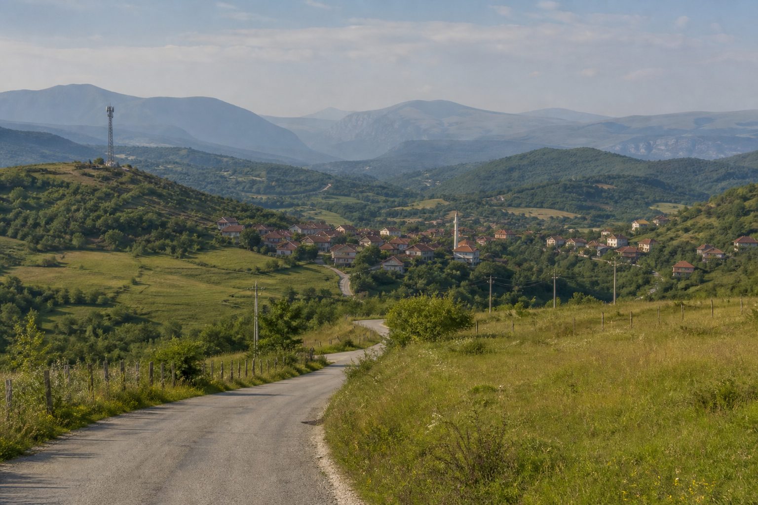 Rolling green countryside in the Western Balkans with a small village and lone cell tower in the distance.