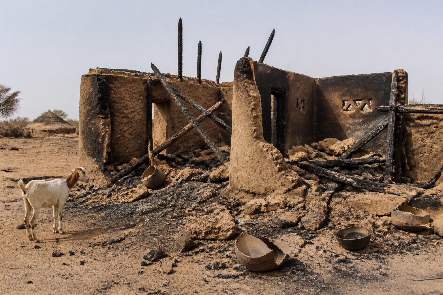 Blackened mud-brick compound ruins in a Sahelian village after a strike.